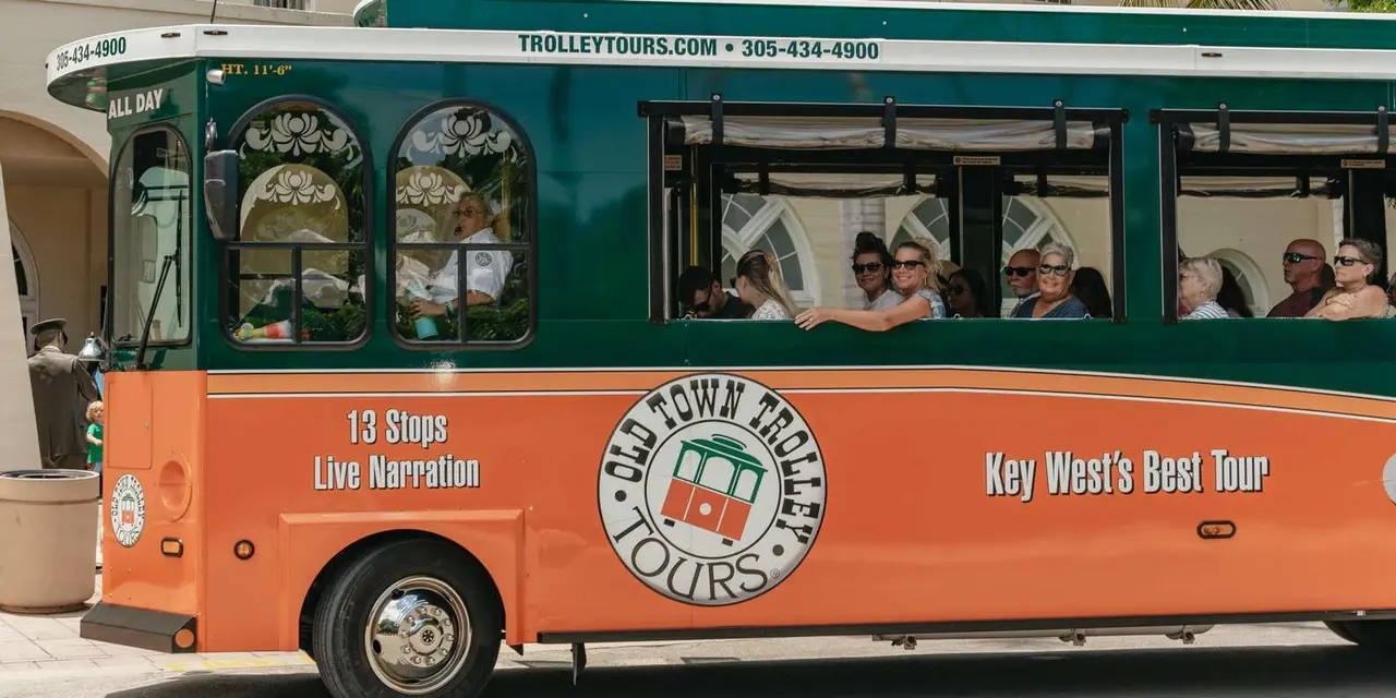 An orange and green Old Town Trolley painted '13 Stops, Live Narration' with passengers waving from its open windows