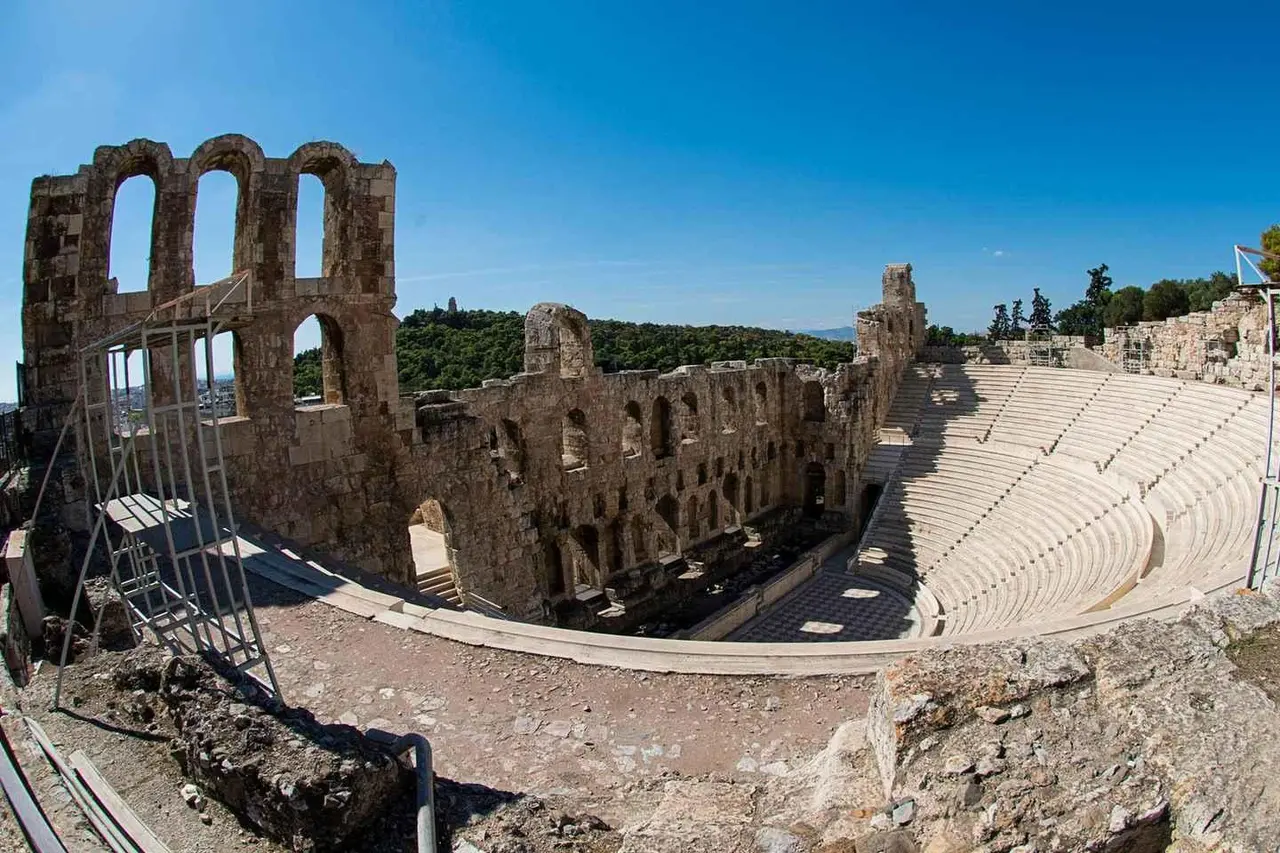 The stone arches and curved marble seating of the Odeon of Herodes Atticus below the Acropolis under a clear blue sky