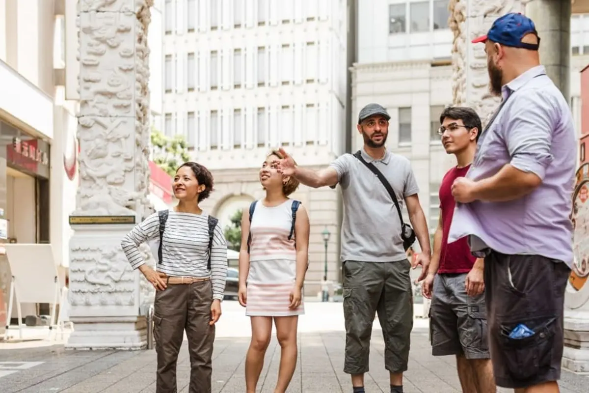 A guide pointing out sights to a small group beside a carved stone gateway