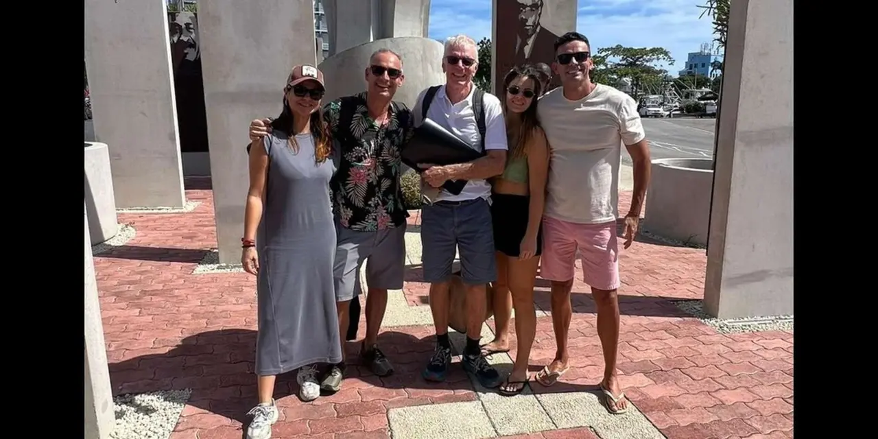 Five visitors posing in front of concrete monument panels on a brick-paved plaza