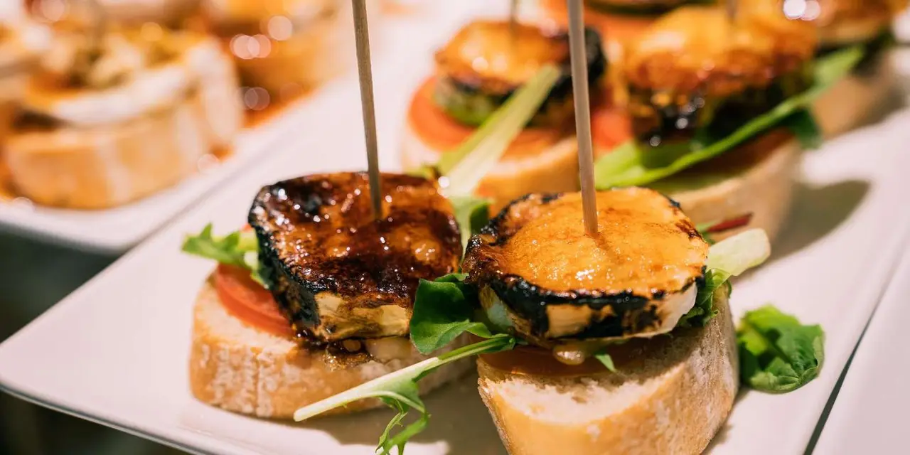 Two skewered toasts of grilled goat cheese on bread with tomato and leaves on a white plate