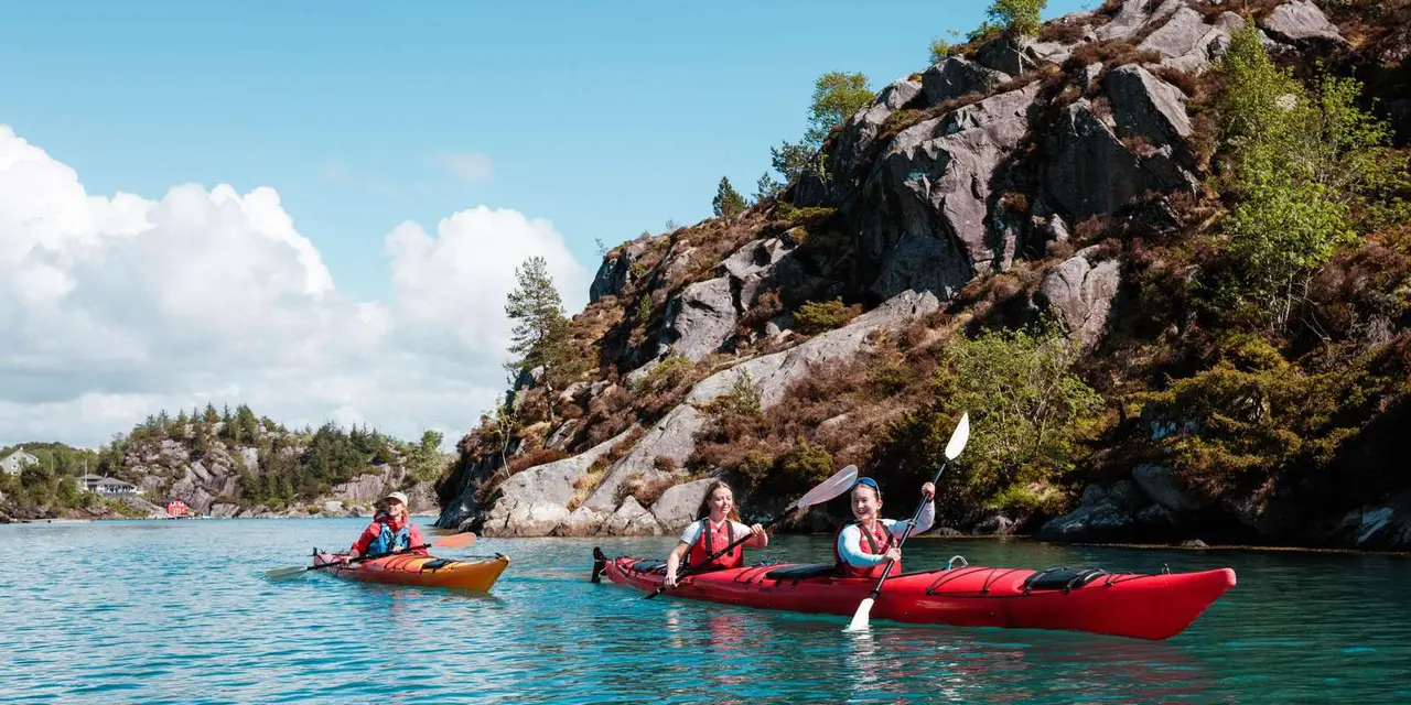 Two red kayaks paddling clear turquoise water beside a rocky, pine-topped island