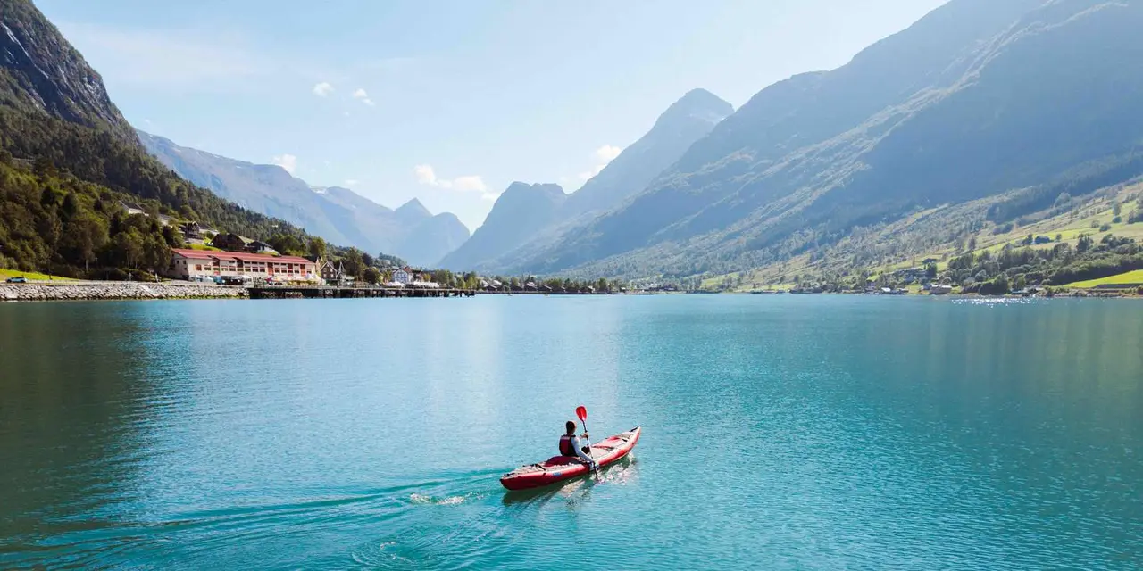 A single red kayak on turquoise fjord water with Olden village and mountains behind