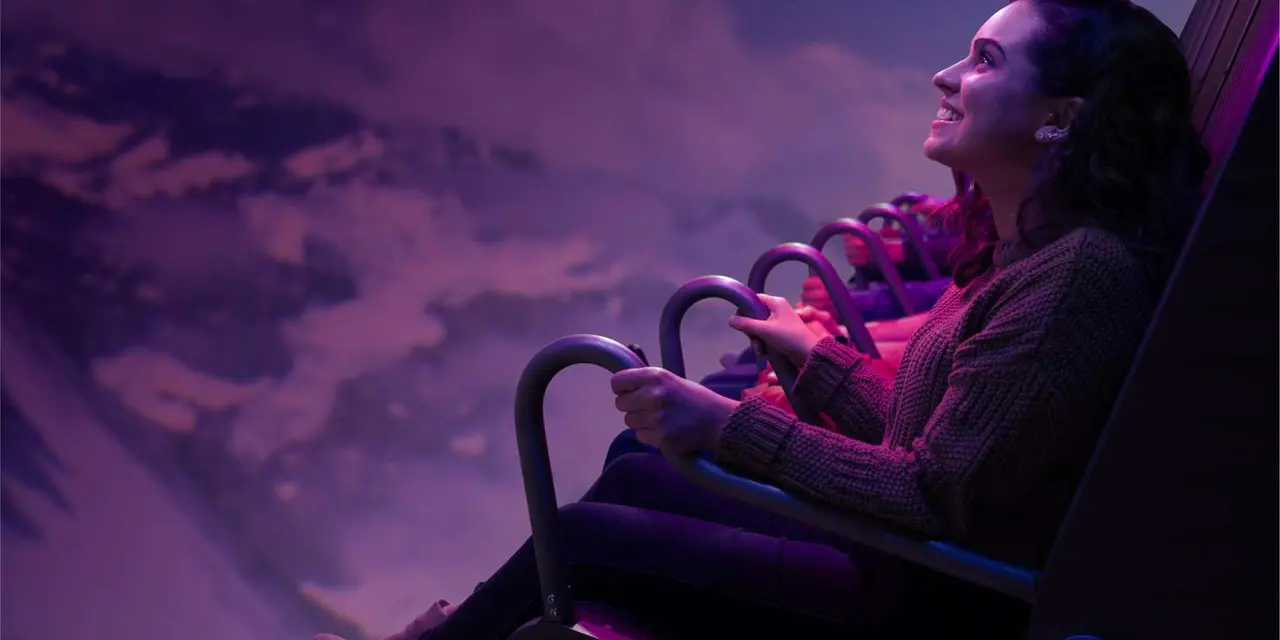 A woman seated in a ride seat gazing up at a purple-lit screen