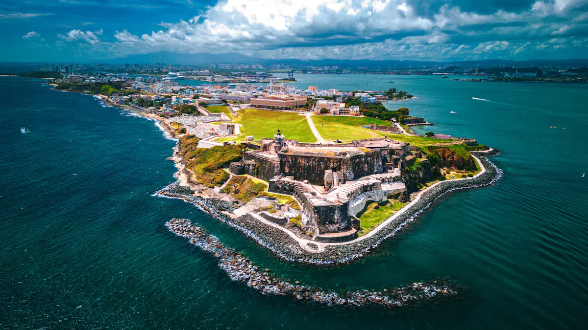 Aerial view of El Morro fort on its grassy headland at the tip of Old San Juan, with turquoise water around it and the city behind