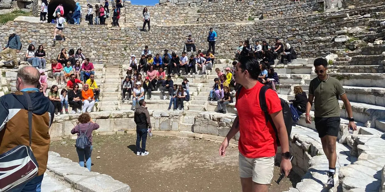 Visitors sitting on the stone tiers of the Great Theatre at Ephesus under a clear blue sky