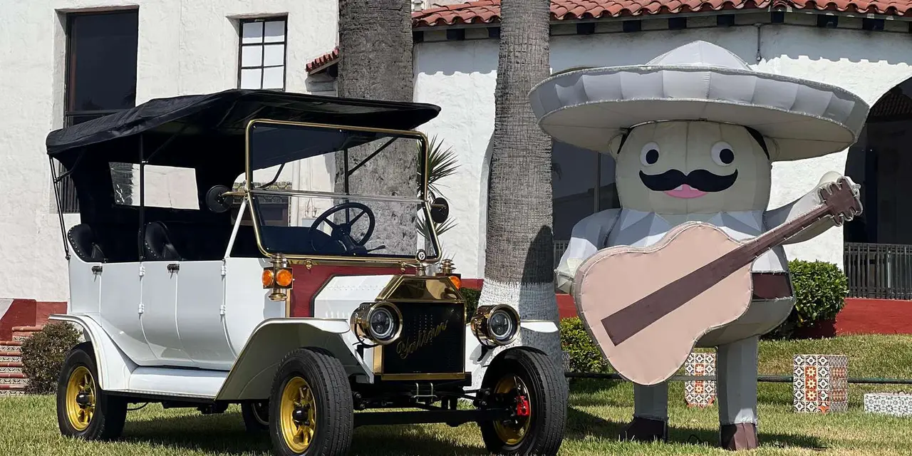 A white open-top Model T replica parked in front of a whitewashed building with a red-tiled roof