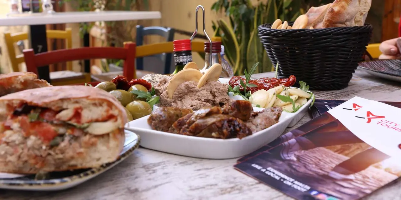 A café table with a stuffed ftira sandwich and plates of Maltese snacks