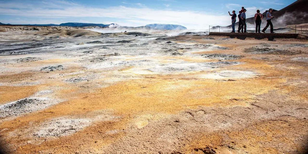 Pale yellow and orange sulphur ground steaming at Hverir, with a small group of visitors on a viewing platform in the distance