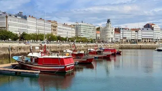 Red fishing boats moored in A Coruña's marina in front of a row of white glass-fronted buildings