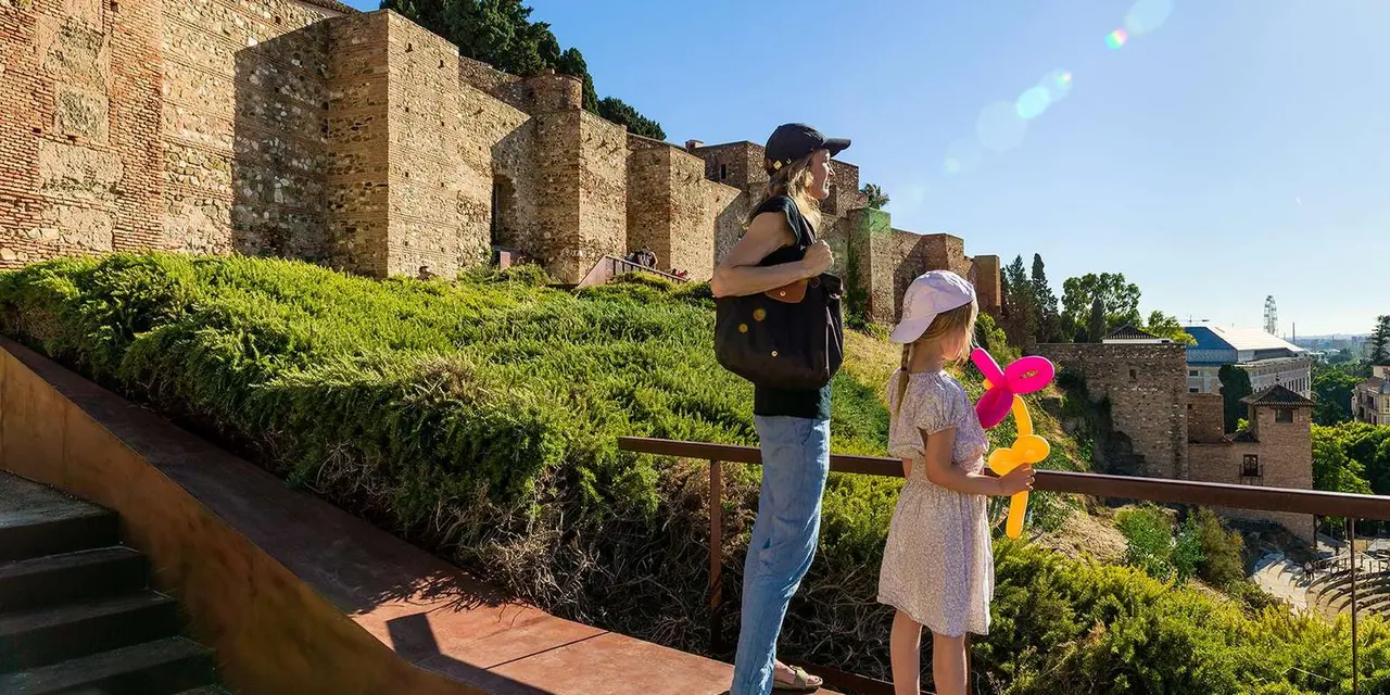 Two visitors on a garden path looking out over the walls of the Alcazaba on a sunny day