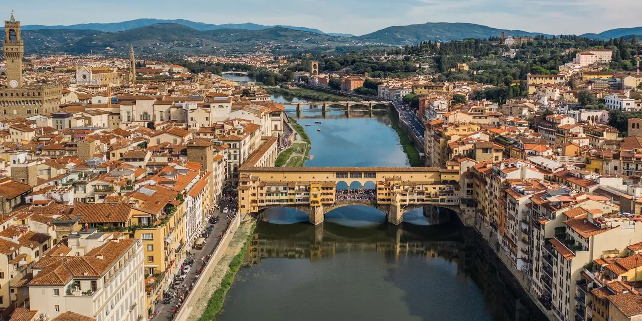 Aerial view of Florence: the Ponte Vecchio crossing the Arno river, with terracotta rooftops and green hills behind