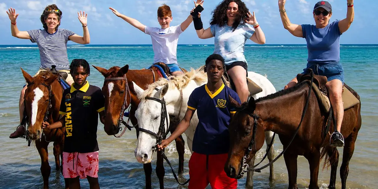 Riders on horses standing in shallow sea water with a guide
