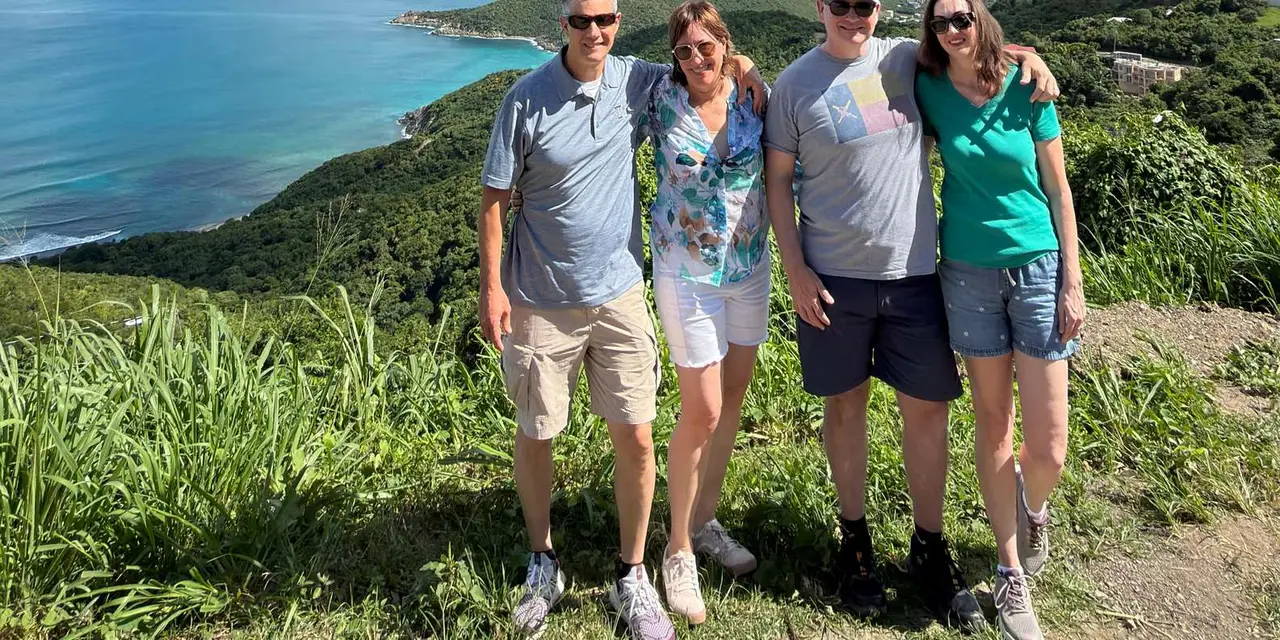 Four visitors posing on a grassy hilltop above turquoise bays and green islands