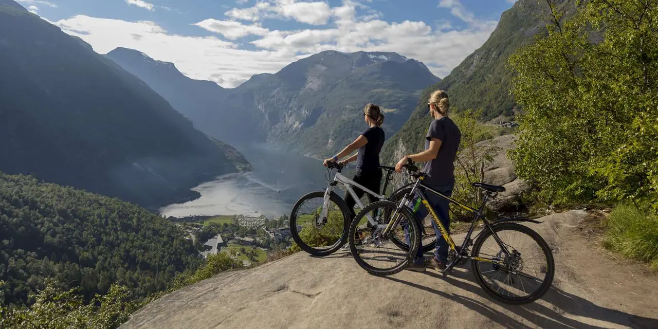 Two cyclists standing with their bikes on a rock high above the Geirangerfjord