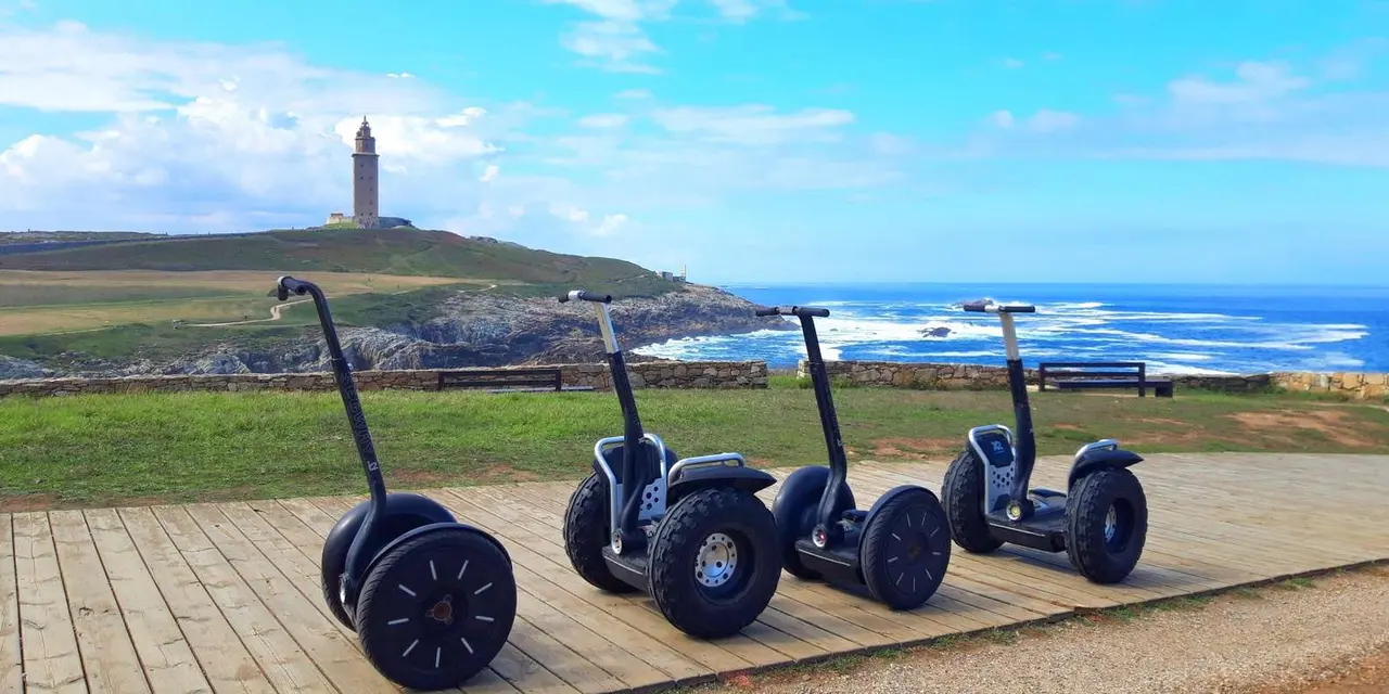Two Segways parked on a boardwalk with the Tower of Hercules on the grassy headland behind