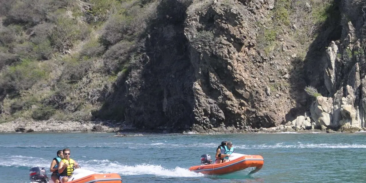 Two orange inflatable speedboats with riders in front of a dark rock cliff