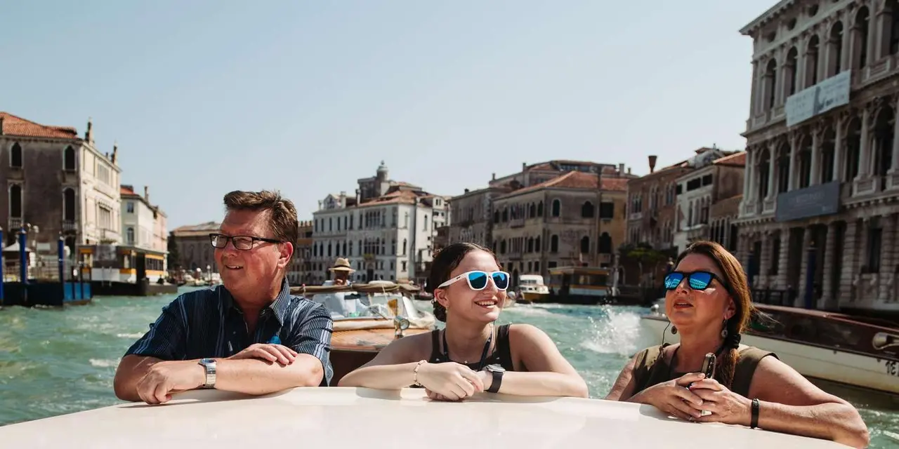 Three smiling passengers leaning on the deck of a wooden motorboat on the Grand Canal
