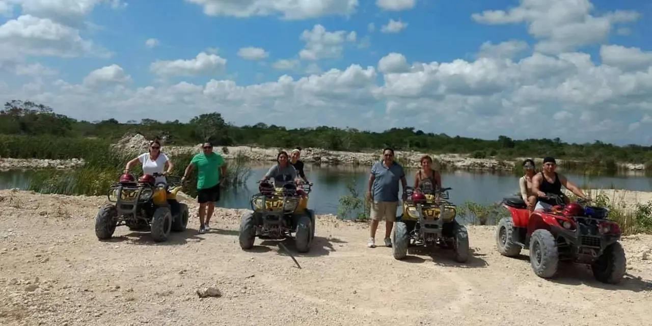 Riders on ATVs parked beside a lagoon under a cloudy blue sky