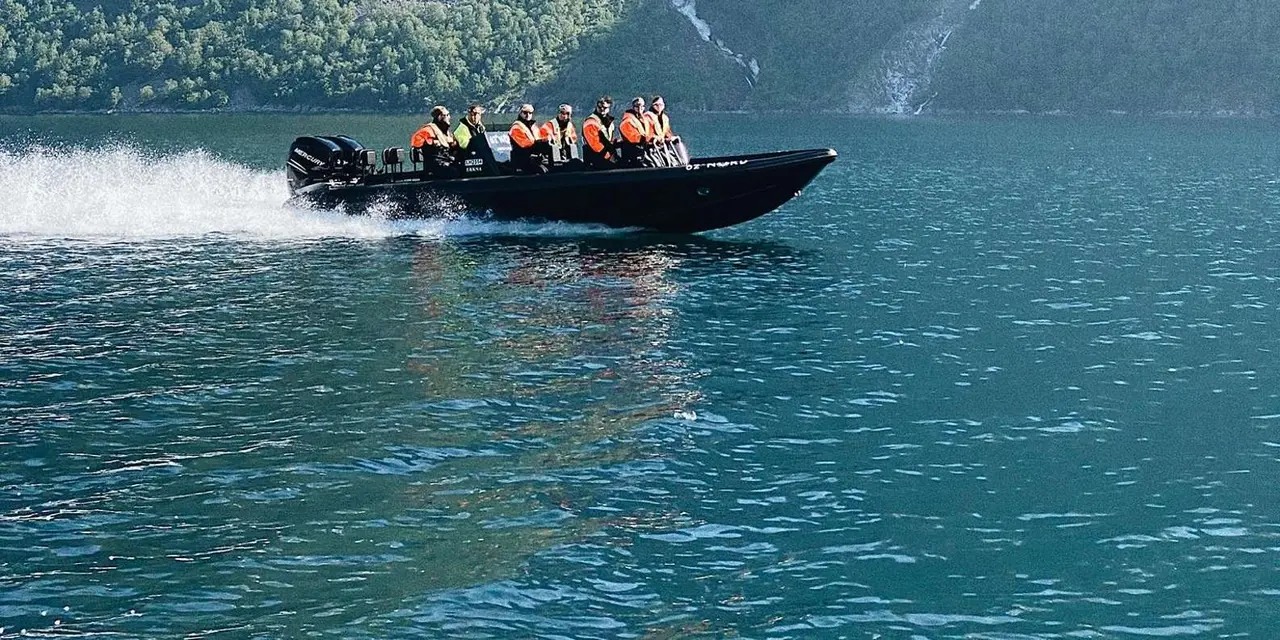 A small inflatable boat with passengers racing along a green, steep fjord shore