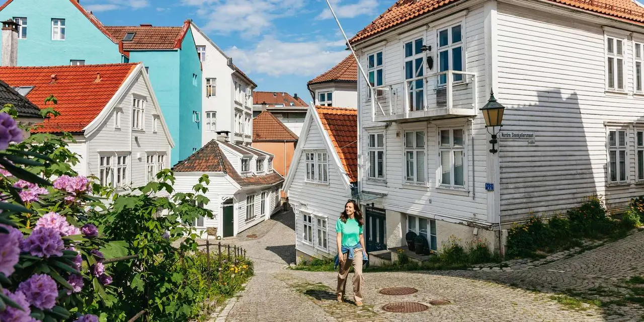 A woman walking up a cobbled lane between white-painted wooden houses with orange roofs under a blue sky