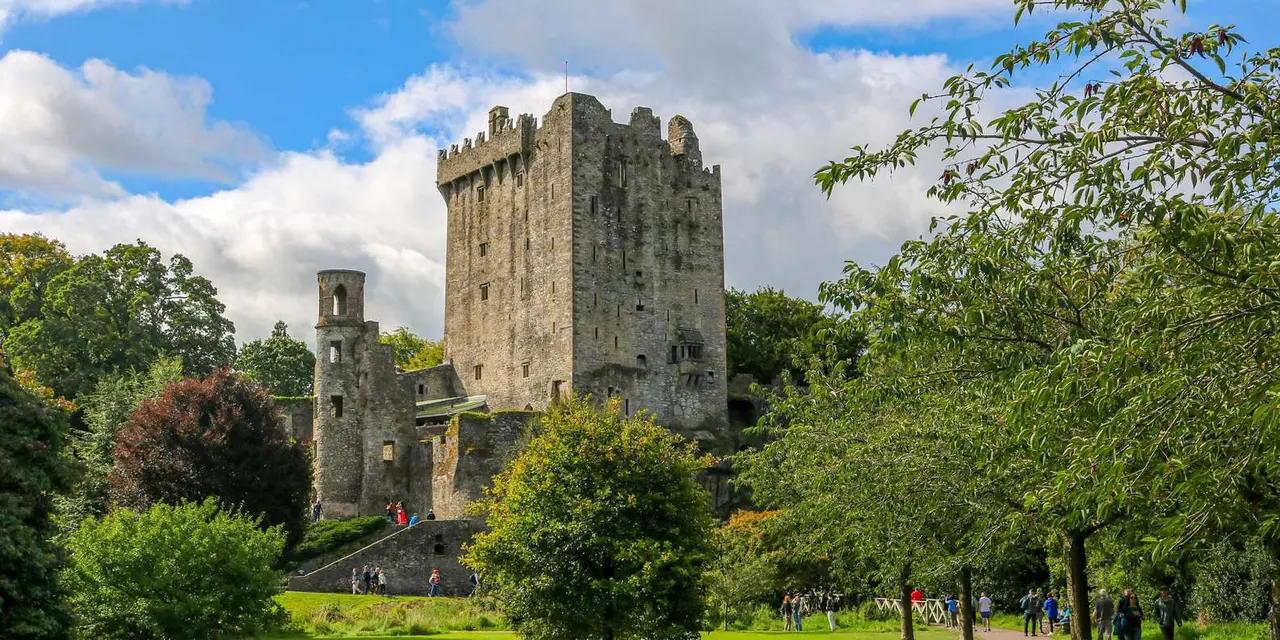 Blarney Castle's tall stone keep rising above green lawns and trees under a blue sky
