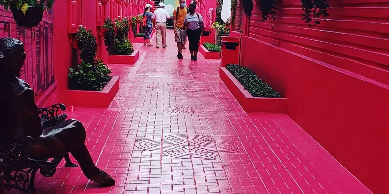 A narrow street with a bright pink painted pavement and pink walls, with people walking in the distance