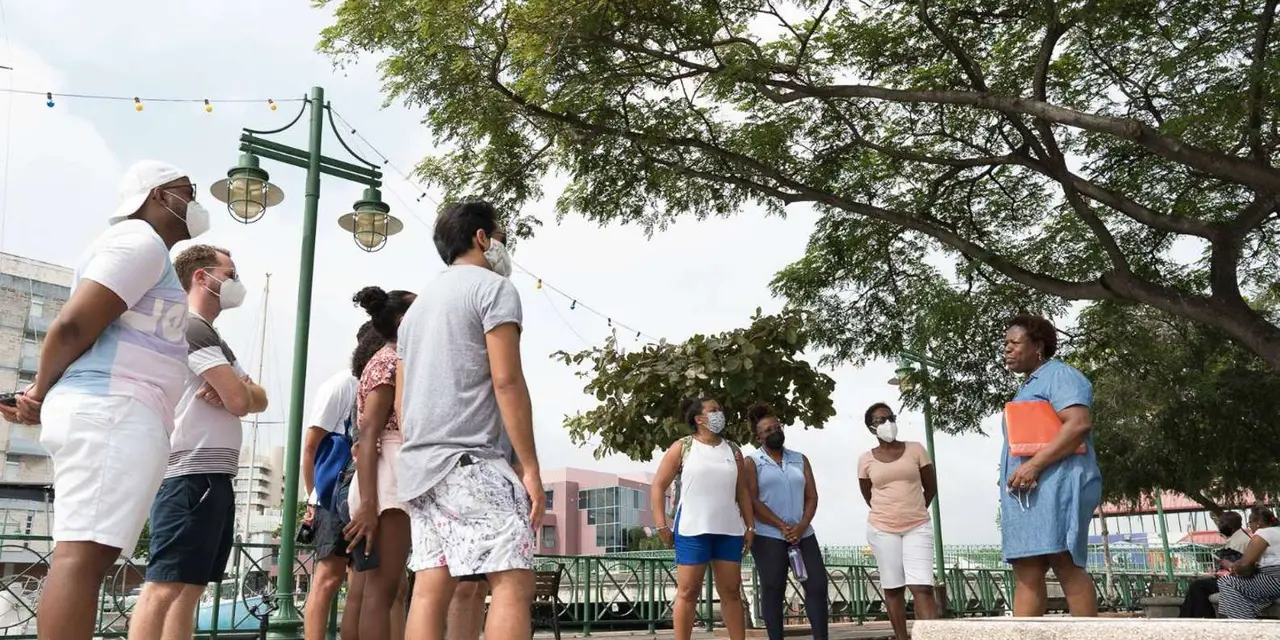 A guide and a small group standing on a waterfront promenade beside harbor boats