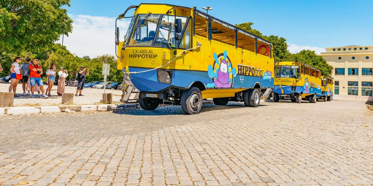 A yellow and blue amphibious tour vehicle parked on cobbles with visitors photographing it