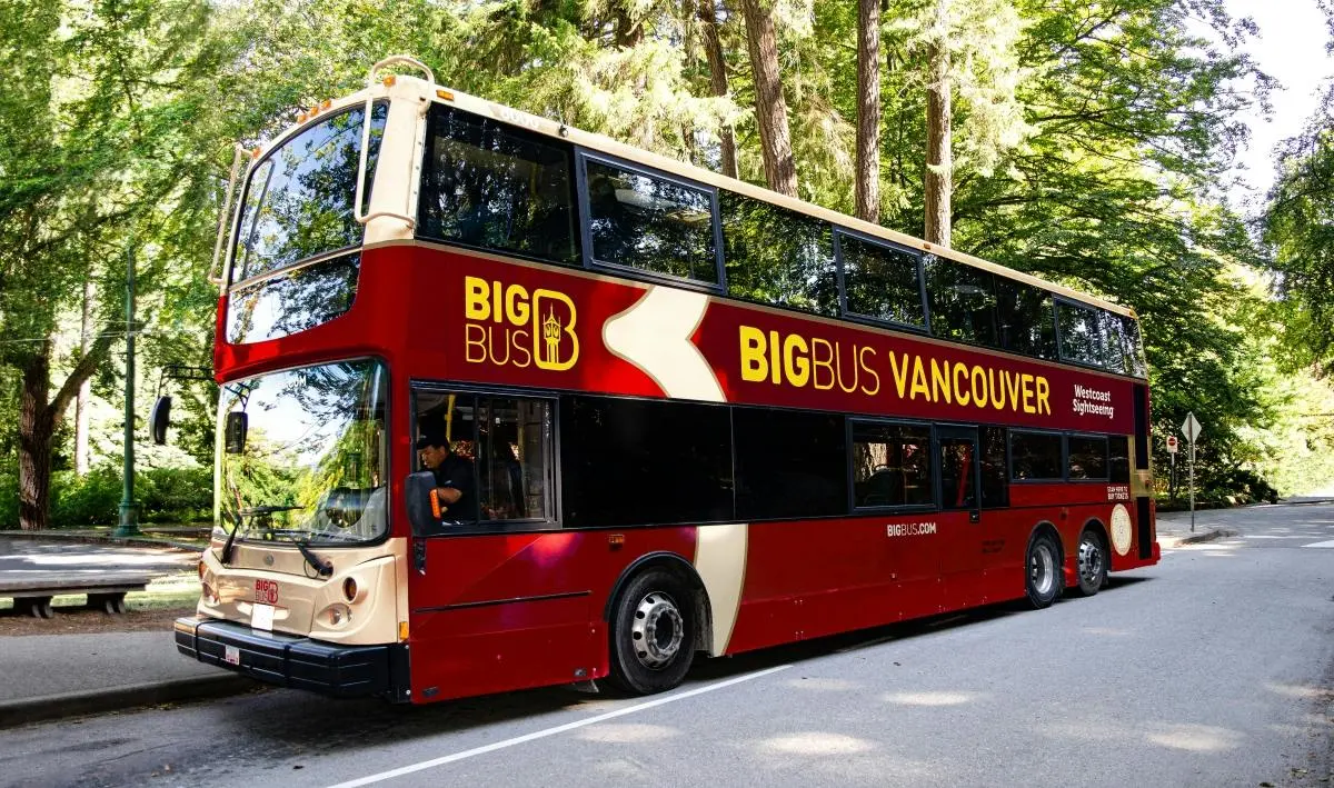 A red-and-cream Big Bus Vancouver double-decker on a road through tall forest