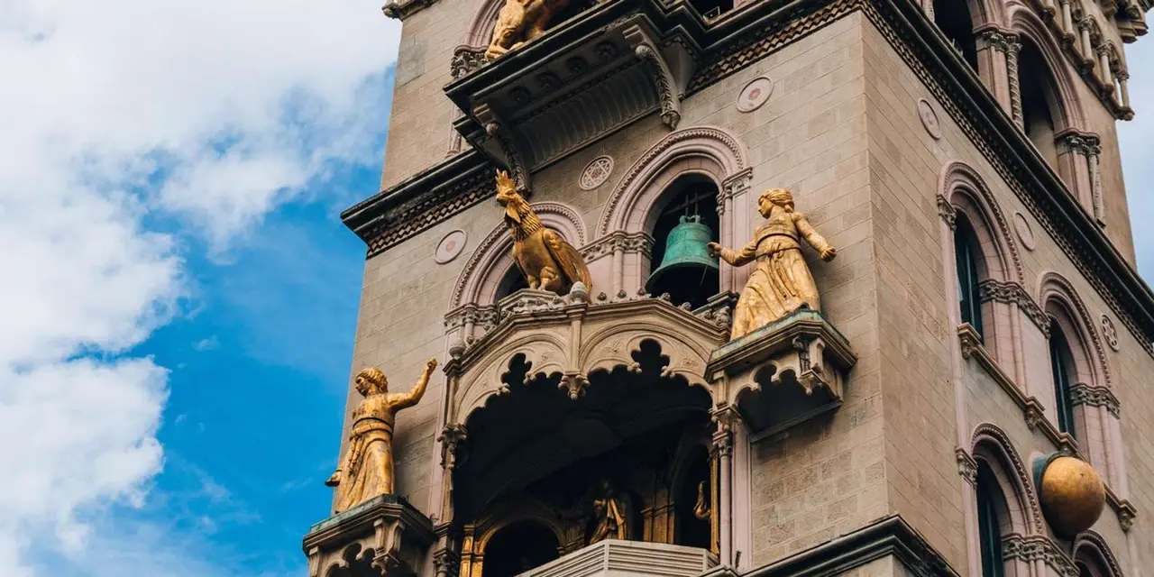 The gilded statues and bells of Messina cathedral's clock tower against a blue sky