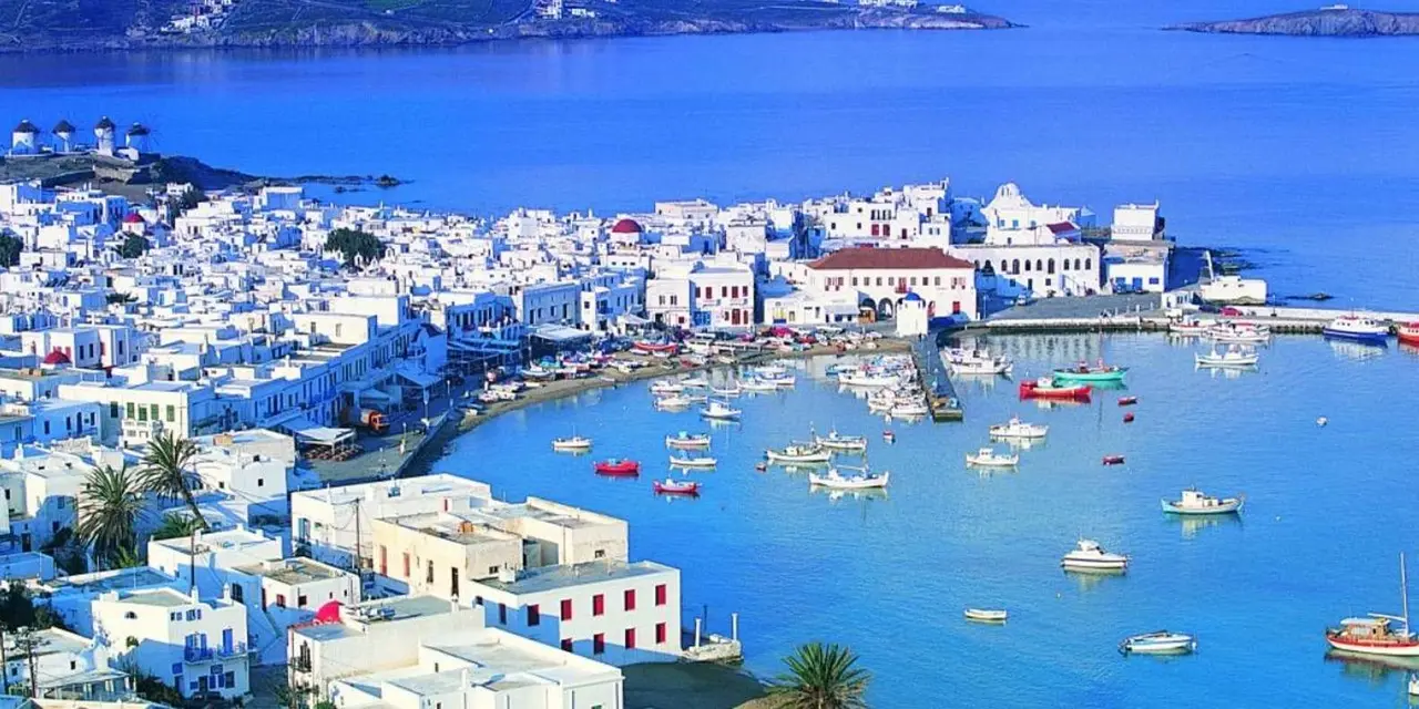 Mykonos Town's white houses curving around a harbour of small boats, with windmills on the far ridge