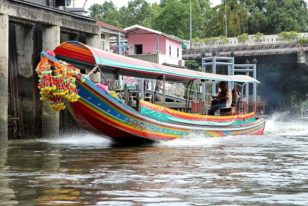 A garlanded long-tail boat speeding along a Bangkok canal