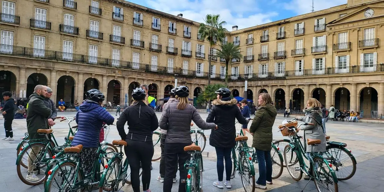 A group of cyclists in coats with green city bikes standing in a stone-arcaded square