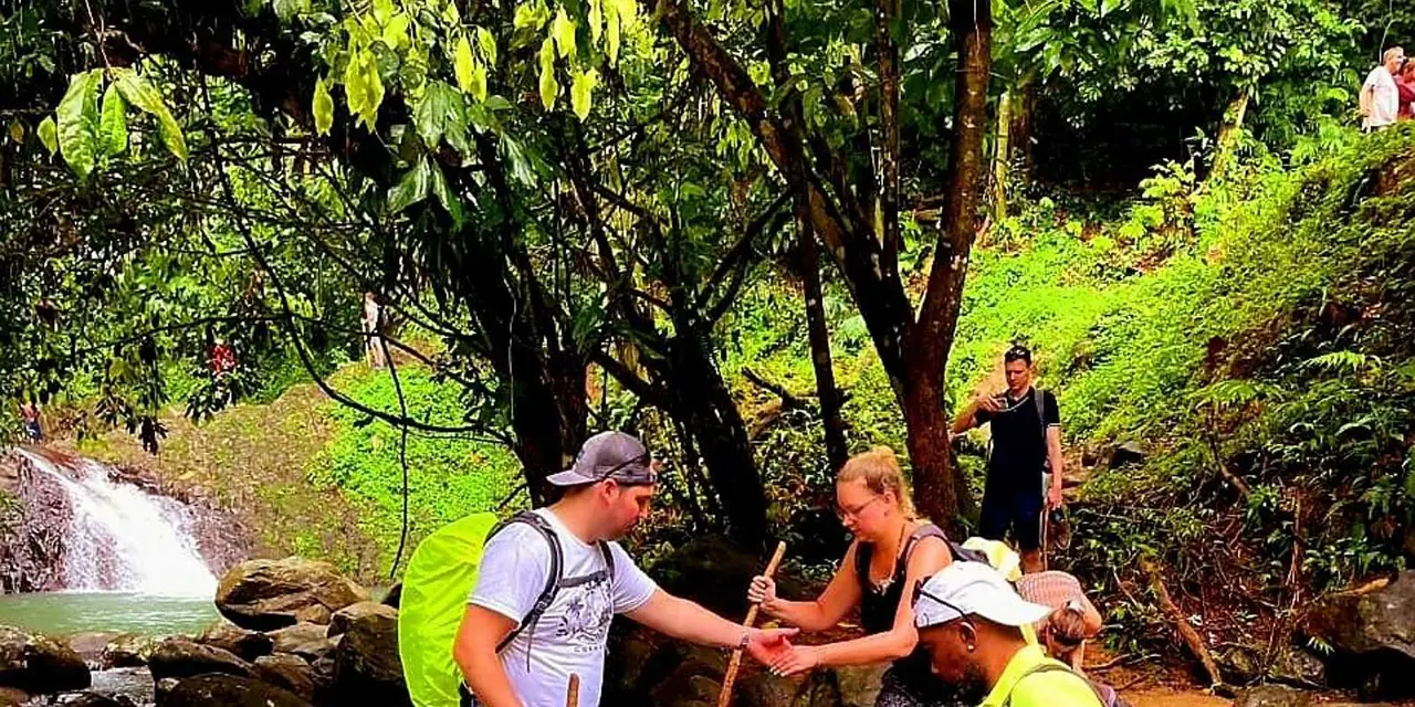 Hikers helping each other across rocks beside a small waterfall