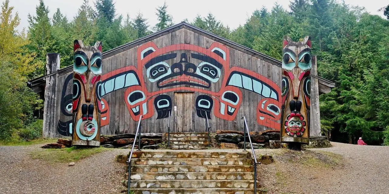 A carved and painted clan house with totem poles at Saxman
