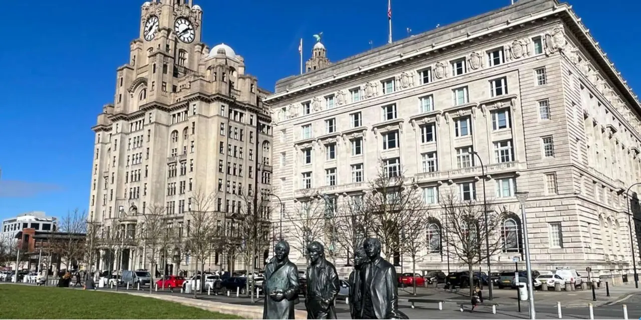 The Royal Liver Building and the Cunard Building rising behind the Beatles statues on Pier Head under a deep blue sky