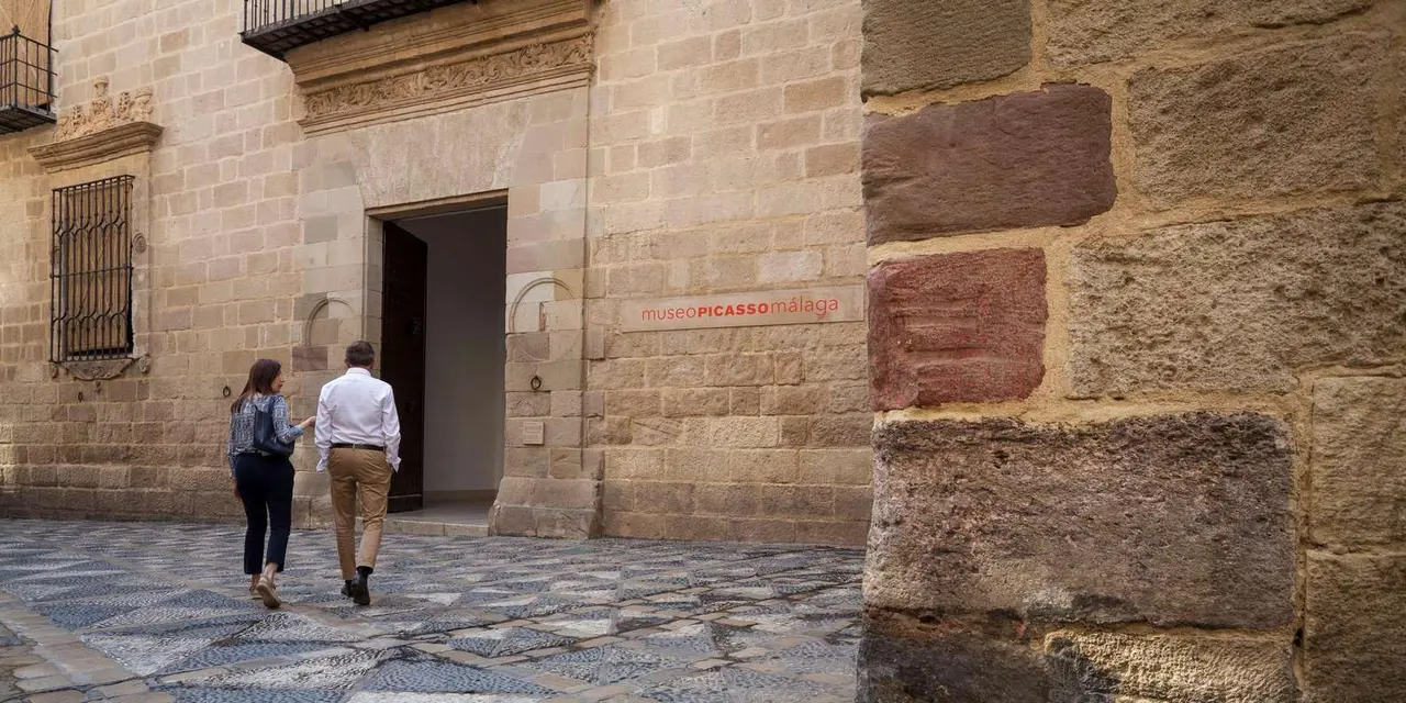 Two visitors walking up to the stone doorway of the Palacio de Buenavista on a patterned cobbled street