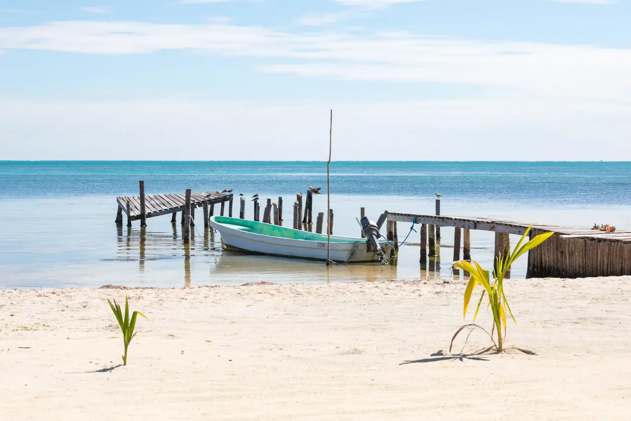 White sand beach on Caye Caulker, about 45 minutes by water taxi from Belize City: a small boat moored between weathered wooden jetties on calm turquoise water under a pale blue sky