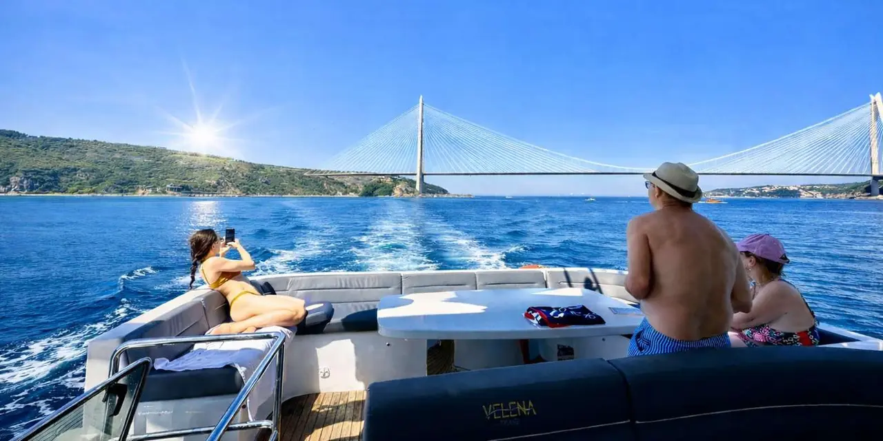 A woman sitting on the bow of a boat speeding up the Bosphorus toward a cable-stayed bridge