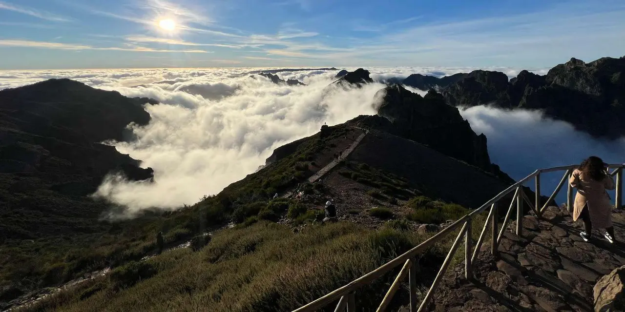 Cloud pooled in a valley below a dark mountain ridge, with a stone stairway and metal railing in the foreground