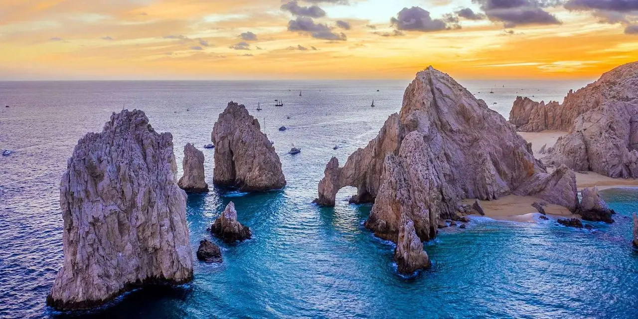 The Land's End rock formations at sunset, with the Arch and pinnacles rising from calm blue water