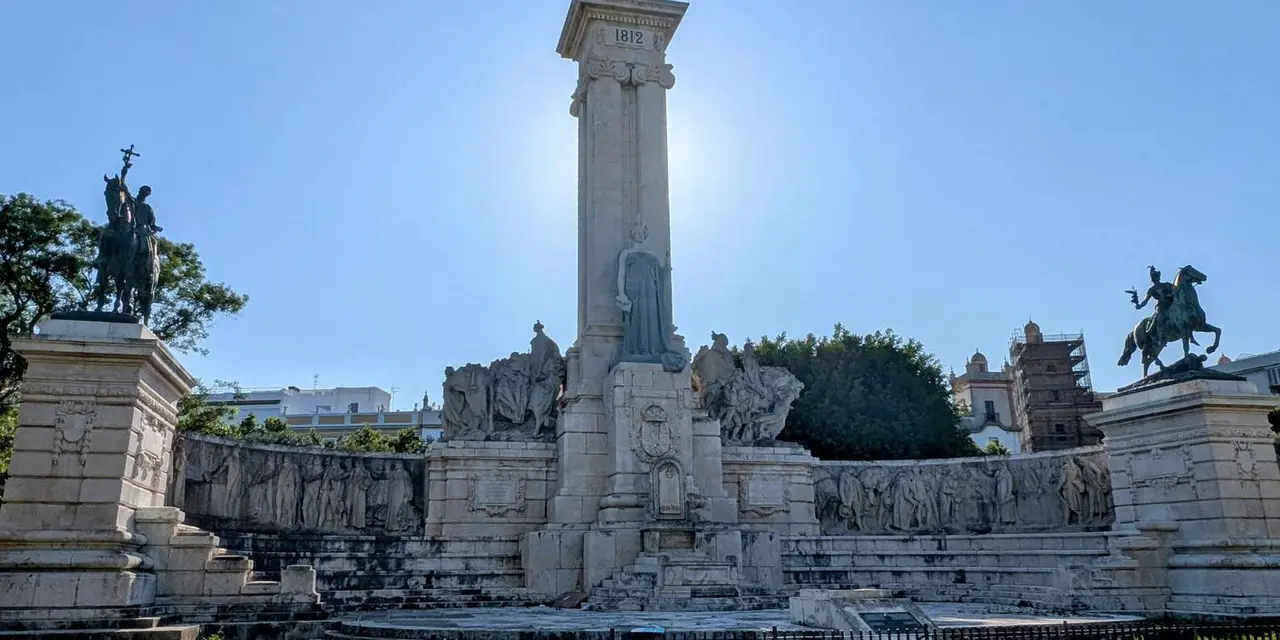 The tall stone column and carved stone relief of the Monument to the Constitution of 1812 against a bright blue sky