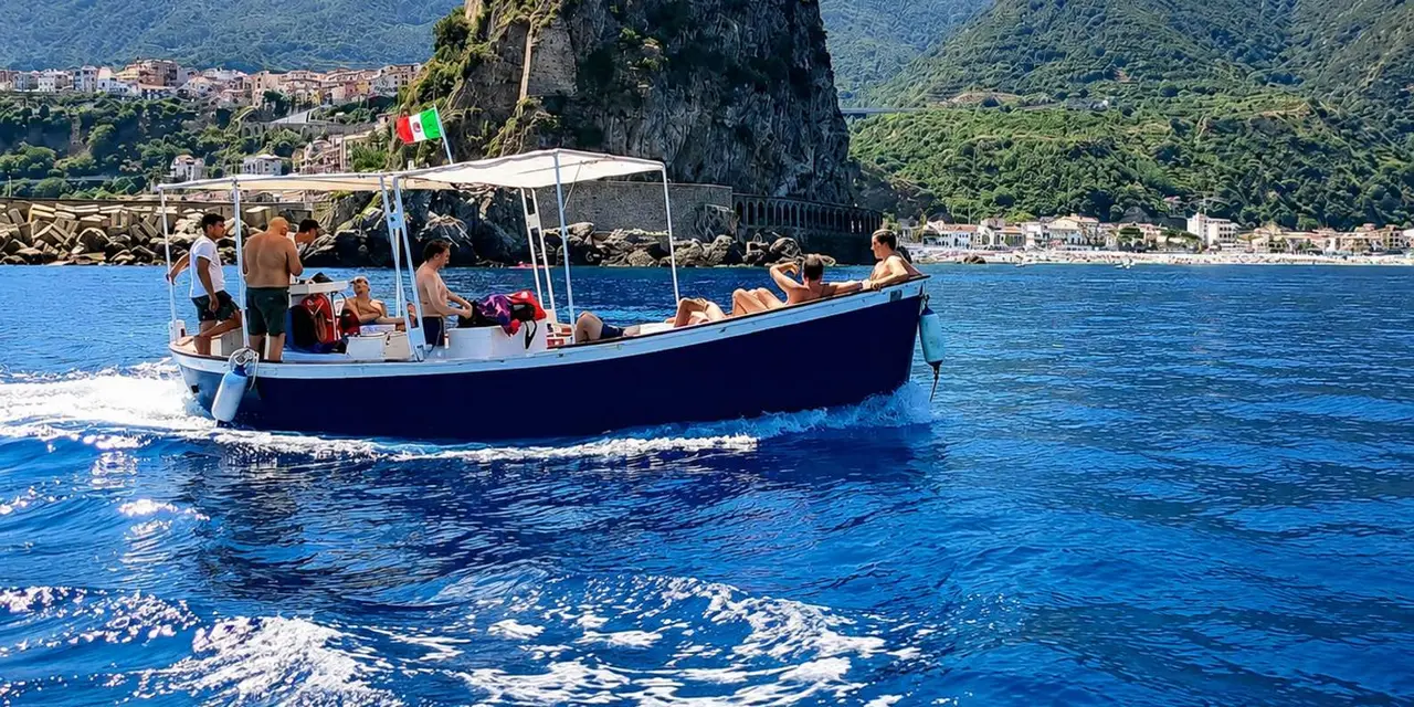 A canopied wooden motorboat with passengers crossing deep-blue water below green coastal cliffs