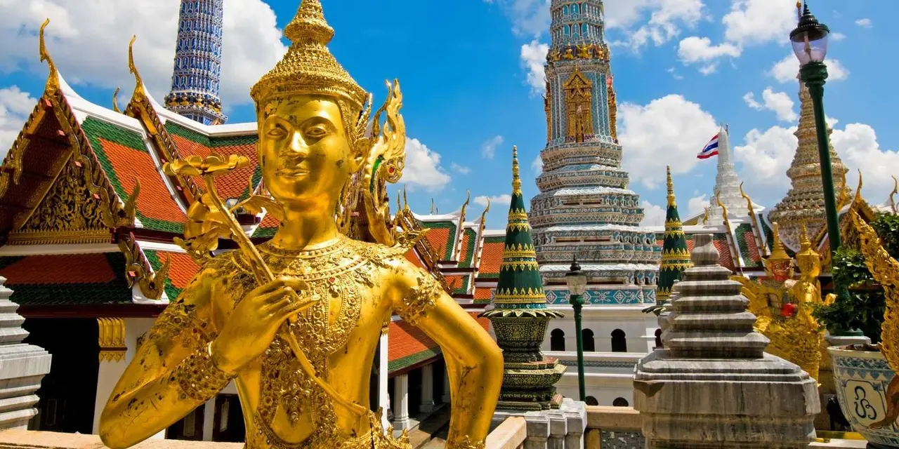 A golden guardian statue in front of the gilded spires of Bangkok's Grand Palace