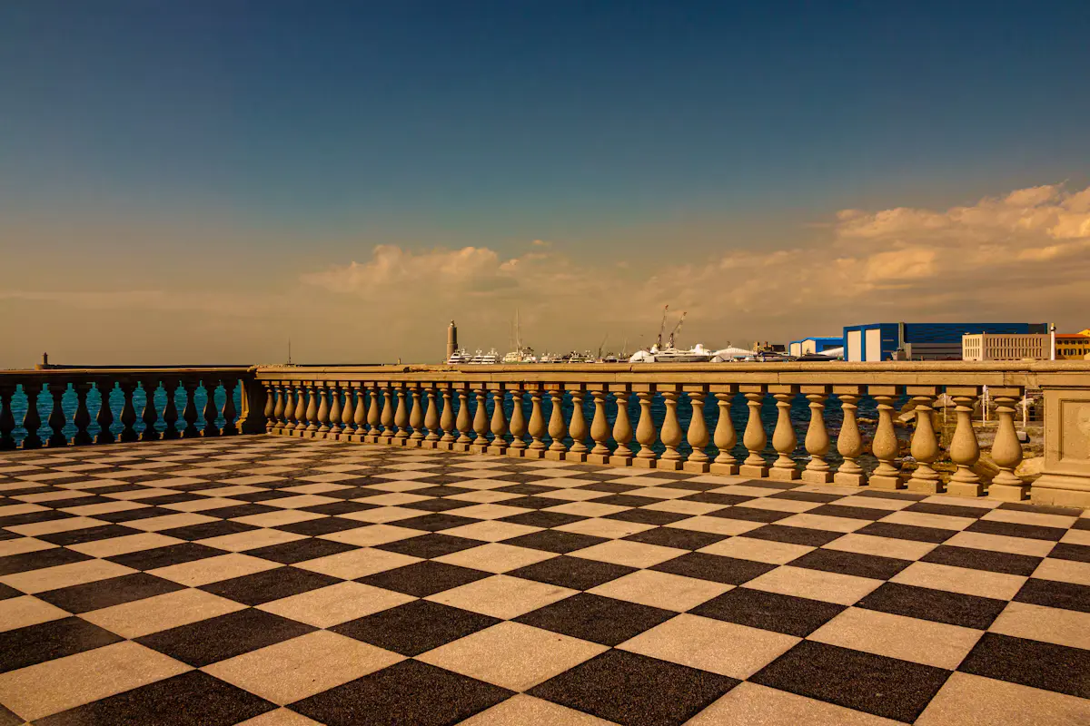 The black-and-white chequerboard paving of Terrazza Mascagni at golden hour, a stone balustrade running along the Livorno seafront under a warm evening sky