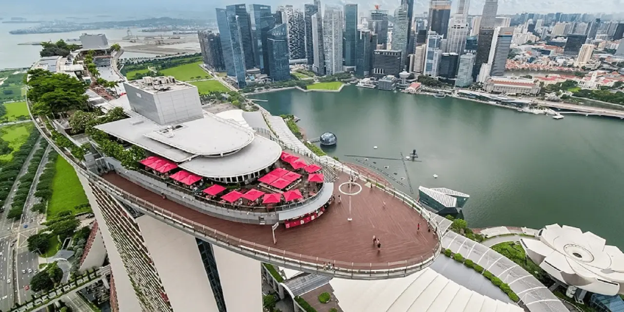 Aerial view of the Marina Bay Sands SkyPark deck with red umbrellas on the rooftop, the city skyline and Marina Bay below