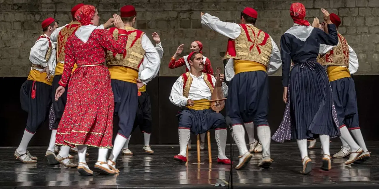 Folk dancers in red, white and gold costume performing on a stone stage