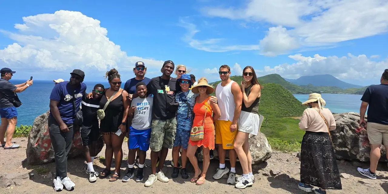 A group of ten visitors posing together on a headland with the green coast behind them