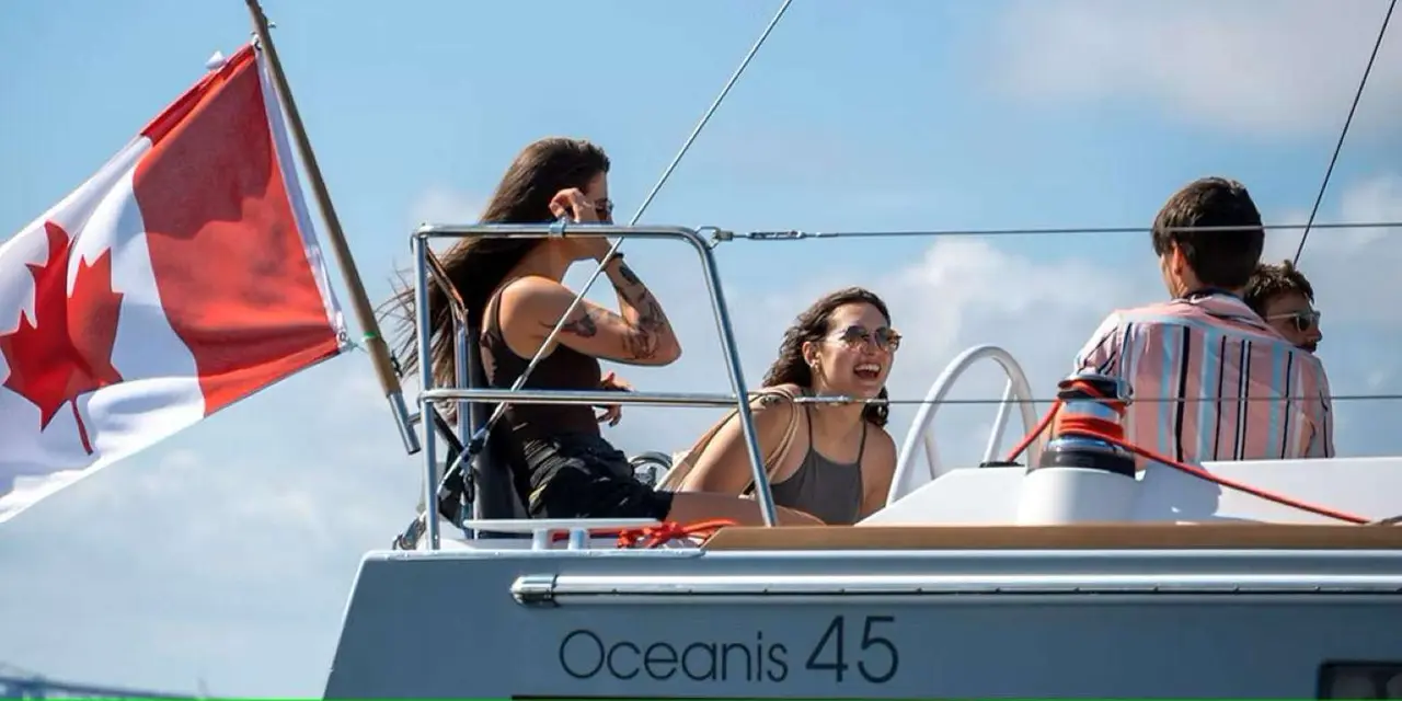 Passengers relaxing on a sailboat's bow under a flying Canadian flag